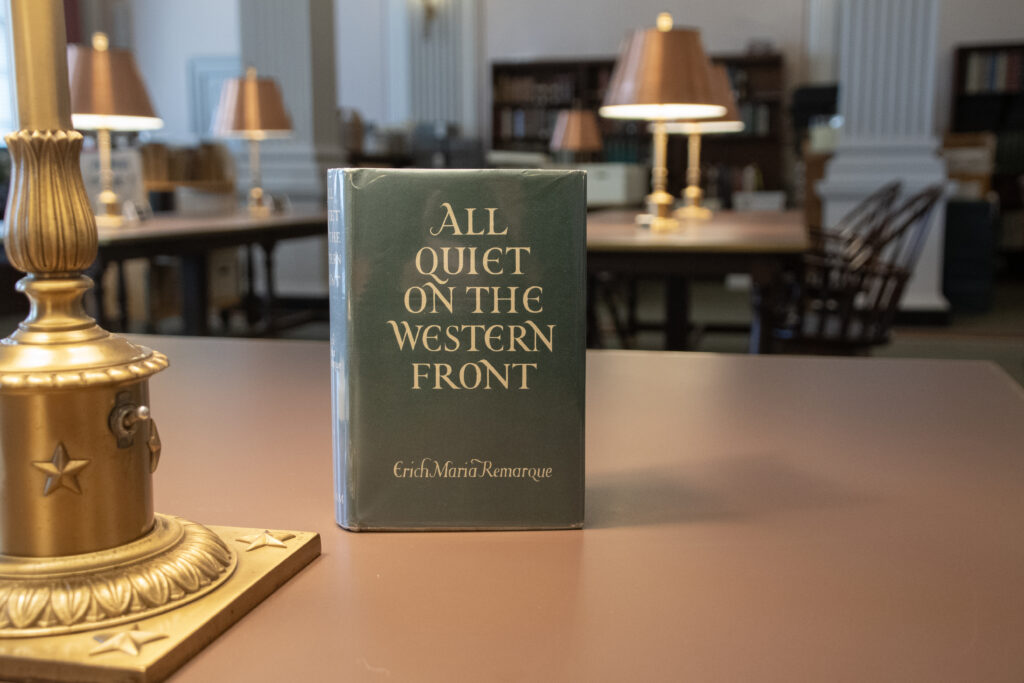 The 1929 edition of All Quiet on the Western Front sits upright on a table. Other tables with lamps appear in the background.